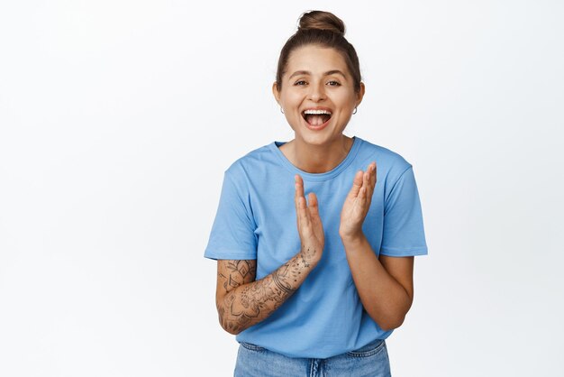 Foto gratuita bella ragazza felice che ride e applaude le mani su sfondo bianco che indossa una maglietta blu