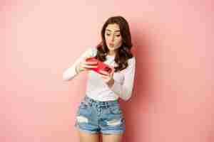 Free photo happy beautiful girl playing mobile video game, holding smartphone horizontally, watching on cellphone with excited face, pink background