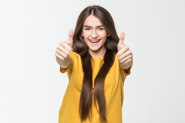 Happy beautiful girl showing thumbs up symbol by two hands isolated on white wall