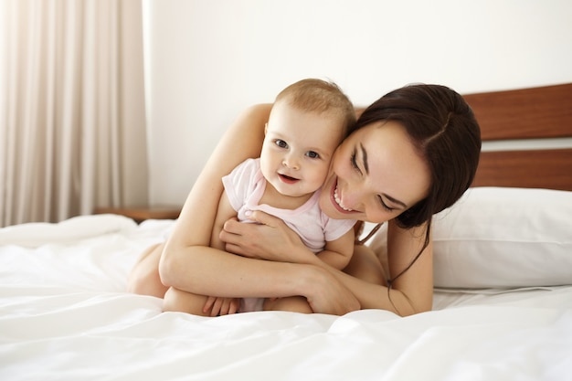 그녀의 아기 딸 웃고 함께 침대에 누워 잠옷 행복 아름다운 어머니.