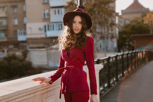 Felice bella donna alla moda in vestito viola che cammina nella via della città, tendenza di moda primavera estate autunno stagione indossando il cappello, tenendo la borsa