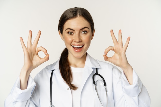 Happy beautiful woman doctor showing okay ok excellent sign smiling amazed approve smth praise stand...