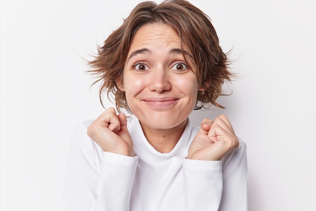 Happy beautiful woman looks with cheerful hopeful expression shakes fists anticipates for good results supports someone dressed in casual jumper isolated over white background. May dreams come true