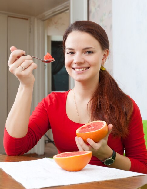Happy beautiful woman in red eats grapefruit