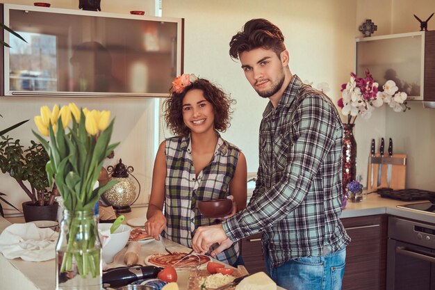 自宅のキッチンで料理をする幸せな美しい若いカップル。