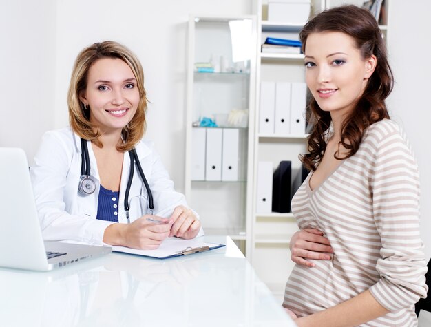 Happy beautiful young pregnant woman and smiling doctor in hospital