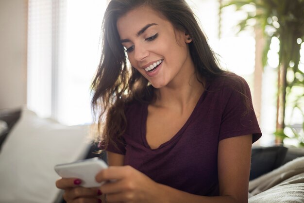 自宅でスマートフォンを持つ幸せな美しい若い女性