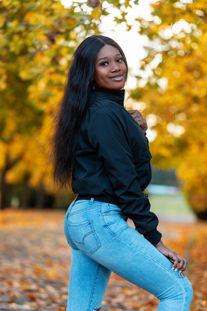 Happy beauty black woman with casual jacket with fashion blue jeans in park with colored yellow autumn foliage Premium Photo