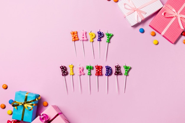 Free photo happy birthday candle sticks with gift boxes and gems on pink backdrop
