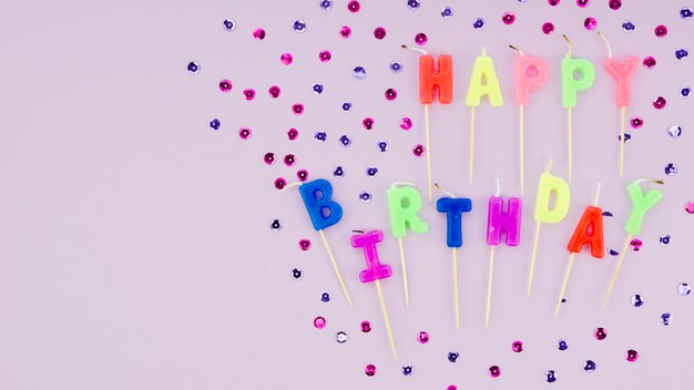 Happy birthday candles and confetti on purple background