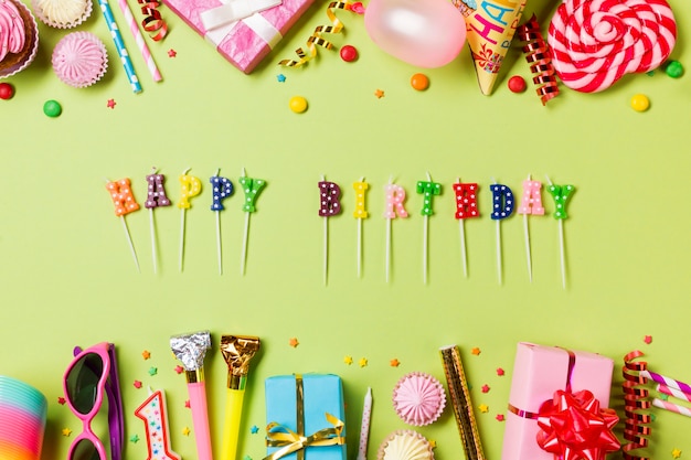 Happy birthday candles with colorful birthday items on green backdrop