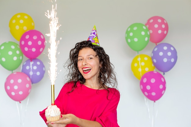 お誕生日おめでとうございます 風船 花火 カラフルな風船 白い背景の上の休日のケーキでポーズをとってセクシーなブルネットの女の子 プレミアム写真