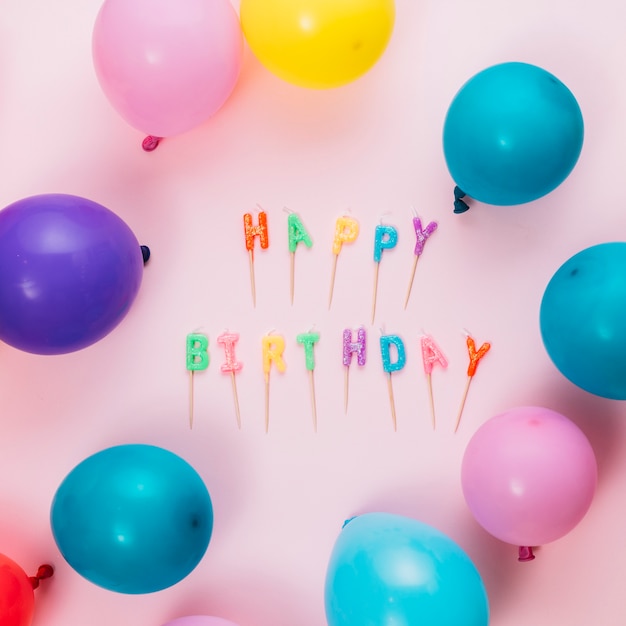 Happy birthday text candles with stick and balloons on pink background