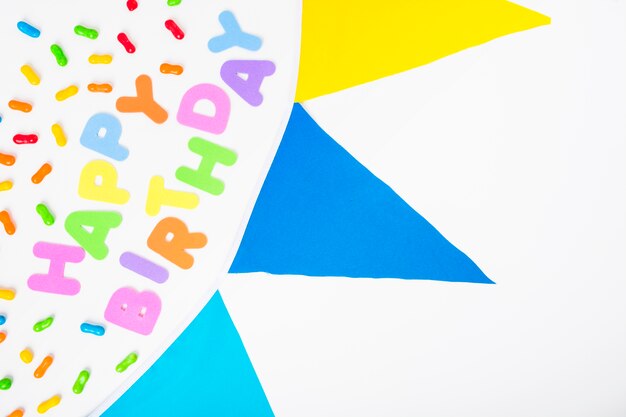 Happy birthday text with candies and bunting on white backdrop