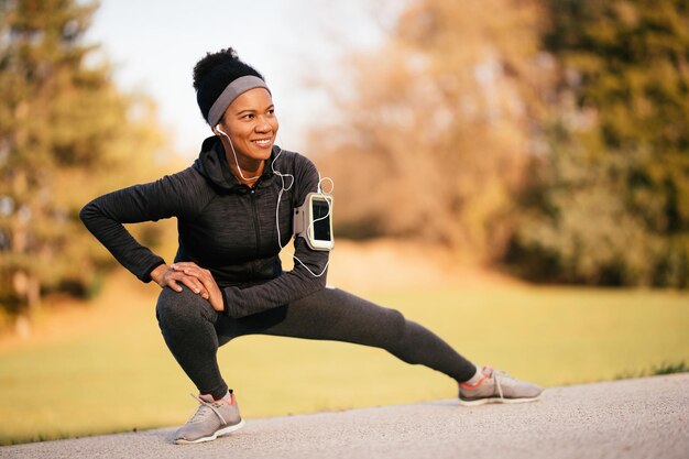 Happy black athletic woman stretching while working out in nature