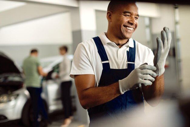 Счастливый черный автомеханик в перчатках во время работы в ремонтной мастерской