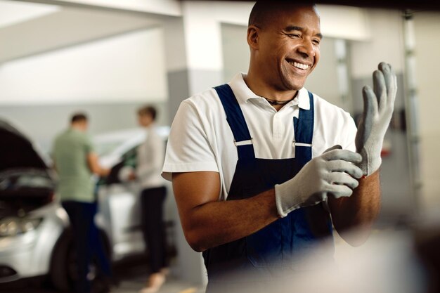 Happy black auto mechanic using gloves while working at repair shop