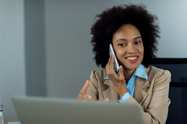 사무실에서 노트북 작업을 하는 동안 전화를 받는 행복한 흑인 여성