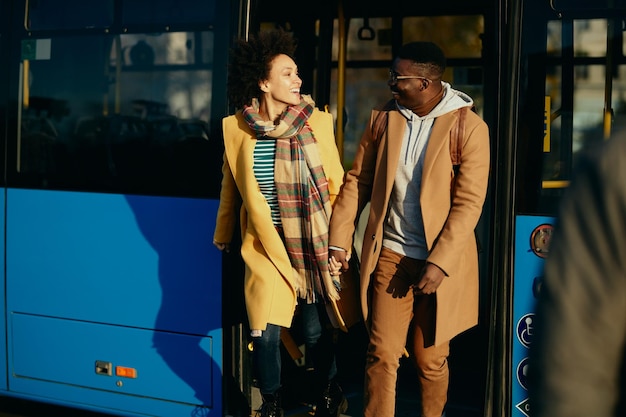 Happy black couple holding hands and talking while getting out of a bus