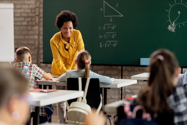 Happy black elementary school teacher taking to her students in the classroom