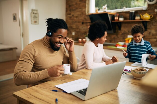 Happy black father drinking tea while having video call over laptop at home