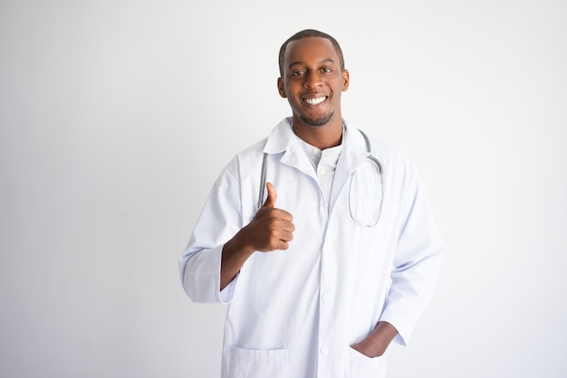 Счастливый черный мужчина-врач показывает палец вверх. Концепция рекламы медицинского продукта.