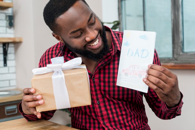 Happy black man holding greeting card and gift