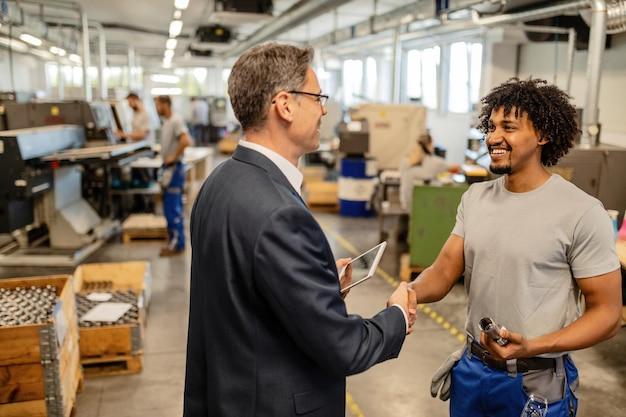 Happy black manual worker shaking hands with company engineer in at factory plant