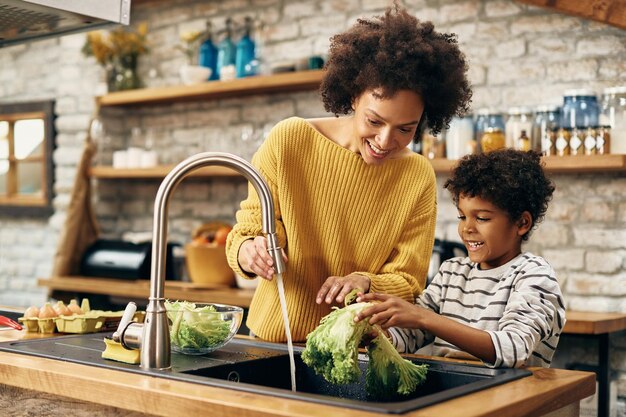 Happy black mother and son cleaning vegetables under kitchen sink