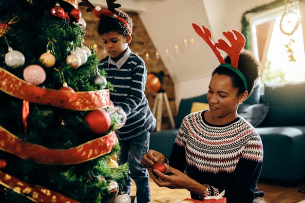 Happy black mother and son enjoying while decorating Christmas tree at home