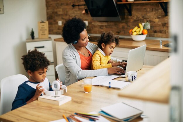 딸이 집에서 무릎에 앉아 있는 동안 컴퓨터 작업을 하는 행복한 흑인 어머니
