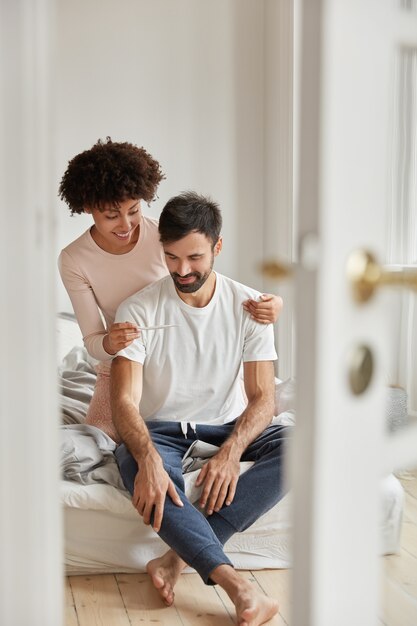 행복한 흑인 여성은 남편에게 임신 테스트를 보여주고 긍정적 인 결과에 만족하고 현대 아파트 침실에서 포즈를 취하고 좋은 소식을 기뻐하며 부모가 될 준비가되었습니다. 실내 가족 커플. 부모