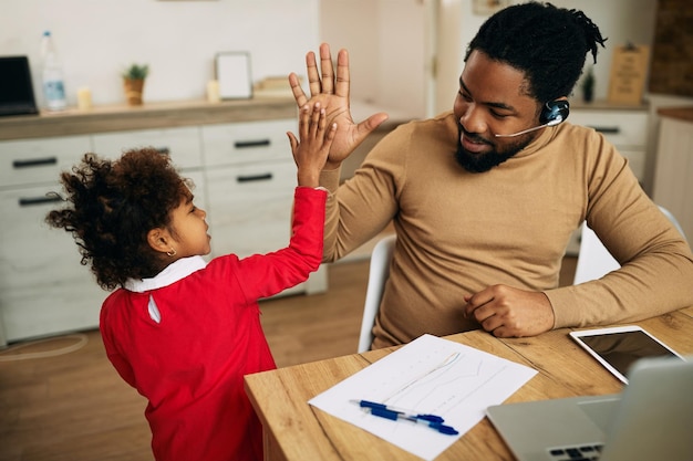 Free photo happy black working father and his daughter giving highfive to each other at home