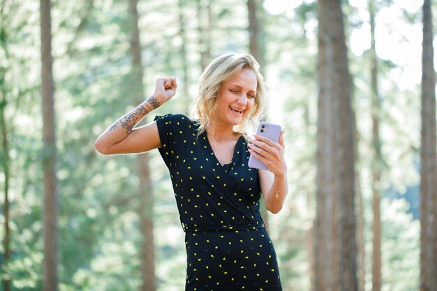 Happy blogger girl is raising up her fist by talking on video call on nature background