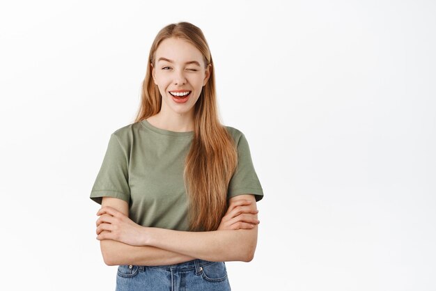 Happy blond girl winking and smiling give you hint encourage standing with crossed arms over chest in confident and relaxed pose white background