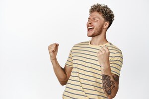Free photo happy blond guy celebrating success making fist pump shouting yes with joy and smiling pleased winning prize and triumphing over victory white background