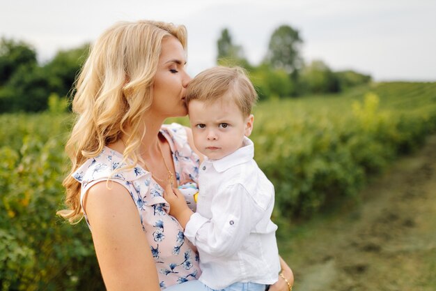 Happy blond woman and cute little boy standing in summer garden