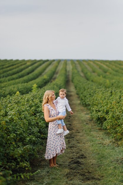 Happy blond woman and cute little boy standing in summer garden