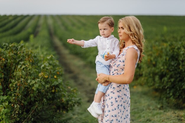 Happy blond woman and cute little boy standing in summer garden