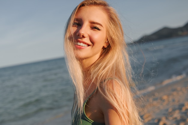 Happy blond woman with perfect smile having fun on sunny beach, looking at camera, running and dancing