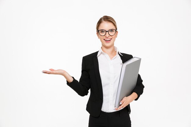 Happy blonde business woman in eyeglasses with folder in hand holding copyspace on the pound and  over white wall