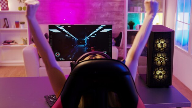 Happy blonde girl winning at a shooter game. She is playing on a powerful gaming computer