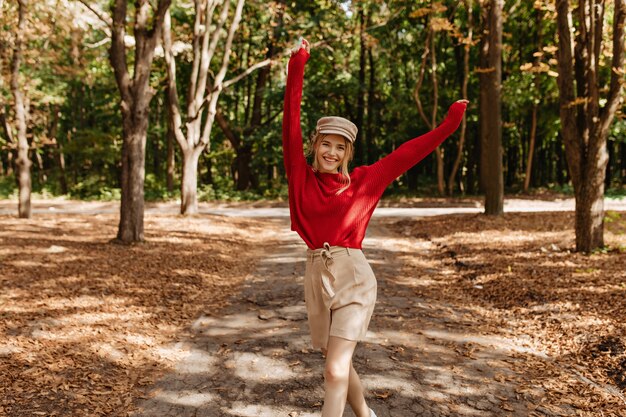 좋은 빨간 스웨터와 베이지 색 반바지 가을 공원에서 춤을 행복 금발 여자. 좋은 weater 야외에서 기쁨으로 포즈 세련 된 젊은 여자.