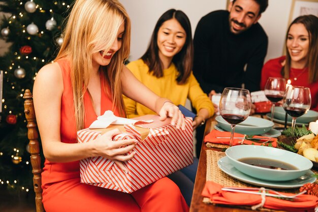 Free photo happy blonde woman opening present at christmas dinner