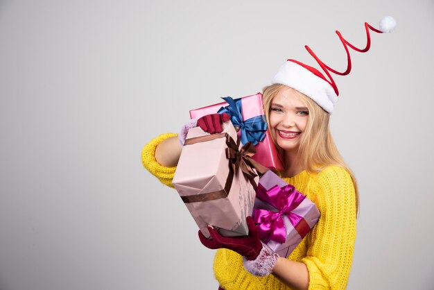 Happy blonde woman in Santa hat holding Christmas gifts.