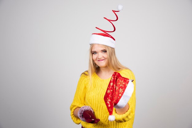 Happy blonde woman in yellow sweater holding Santa hat.