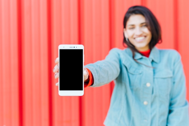 Happy blurred woman showing mobile phone against red metallic background
