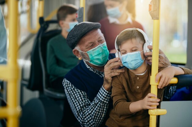 Happy boy enjoying in music over headphones while commuting by bus with is grandfather