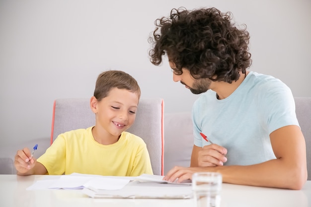 Happy boy and his dad doing school home task together, writing in papers and discussing lesson. Family and gay parents concept