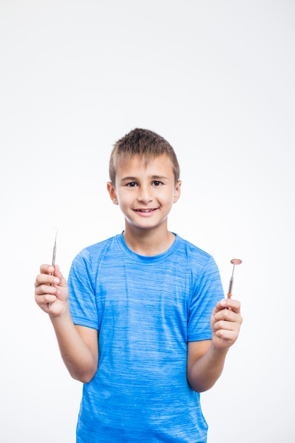 Happy boy holding scaler and dental mirror on white background